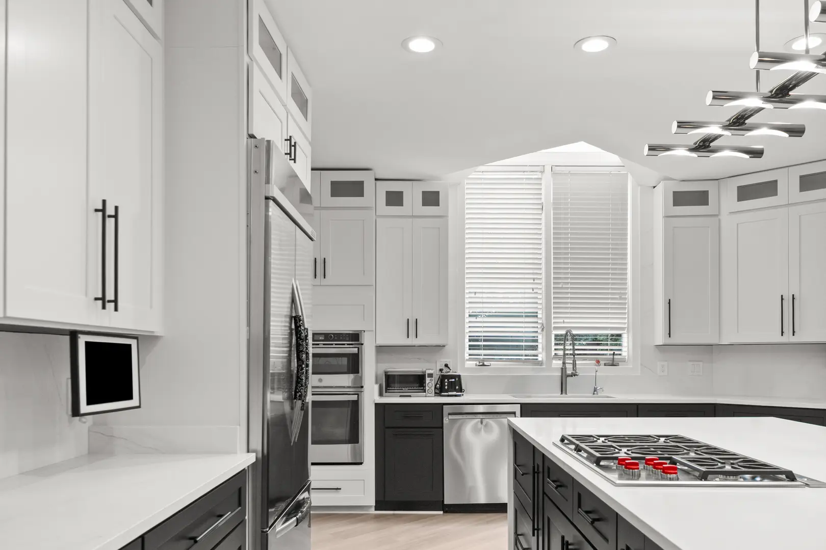 Finished kitchen with white shaker upper cabinets, dark base cabinets, a quartz island with a gas cooktop, double wall ovens and a chrome pendant over the counter