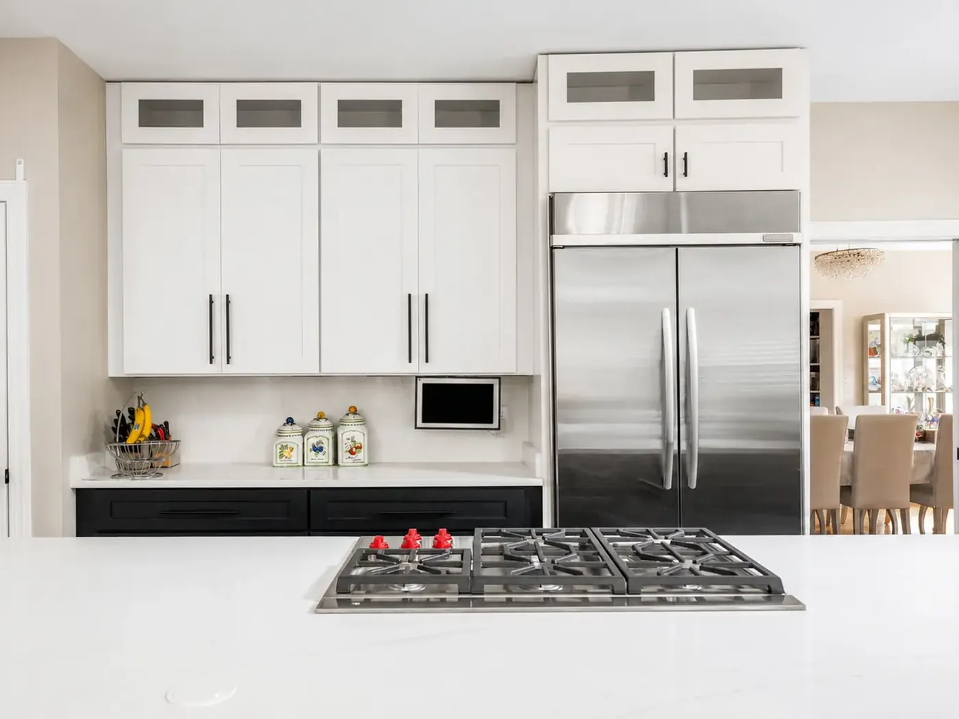 Remodeled kitchen with white shaker cabinets, a gas cooktop in the quartz island and a stainless refrigerator