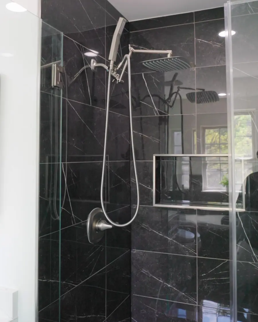 Black marble tile shower with a glass door, rain head and handheld shower